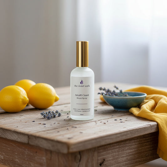 White room spray bottle with gold lid, labeled Amalfi Coast on a wooden table and lemons, dried lavender flowers.