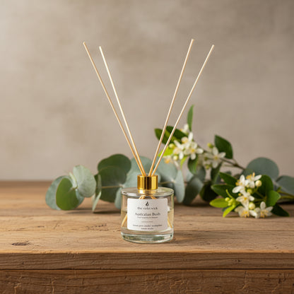 clear diffuser bottle with gold lid on wooden bench and eucalyptus leaves, lemon myrtle in background
