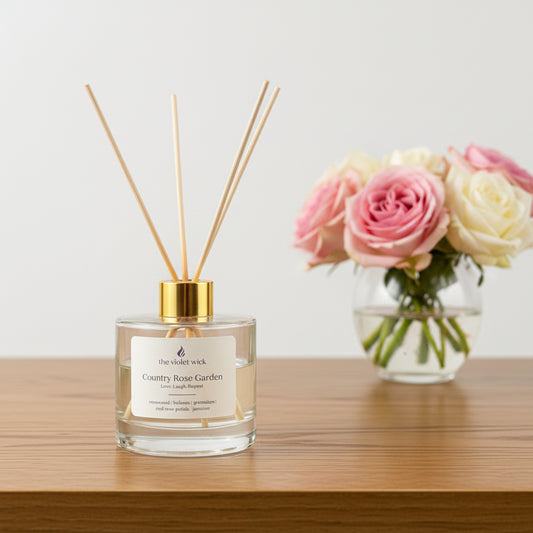 Country Rose Garden Reed Diffuser by The Violet Wick on coffee table with vase of roses.
