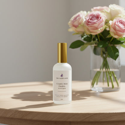 Bottle of 'Country Rose Garden' room spray on table with vase of pink roses.