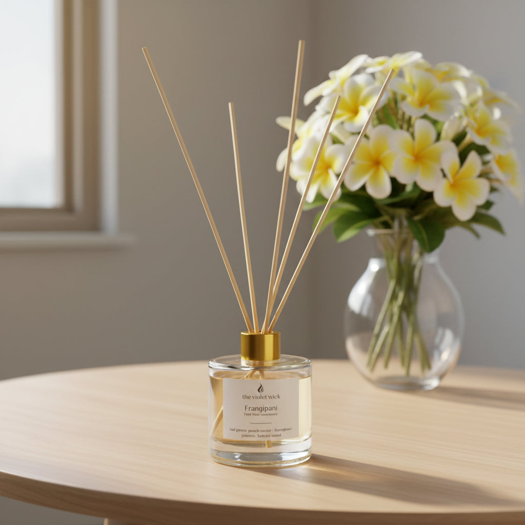 clear reed diffuser bottle labeled Frangipani on a coffee table with a vase of frangipani
