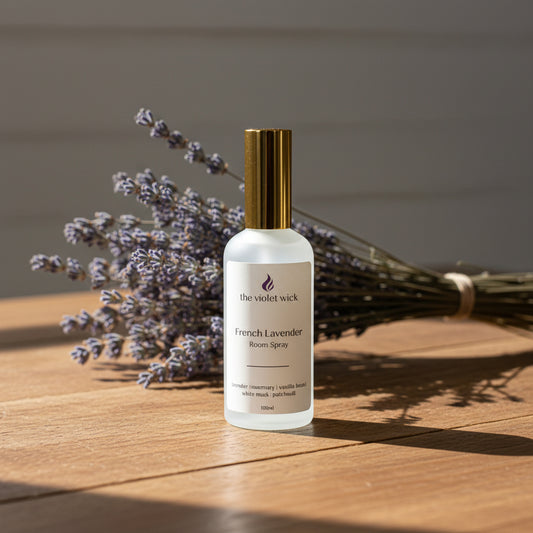 Bottle of French Lavender room spray with a gold cap on a wooden table and dried lavender.