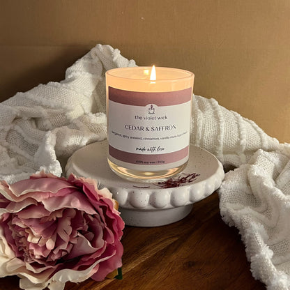 Cedar & Saffron scented soy candle from The Violet Wick in glass jar with pink flower and white throw.
