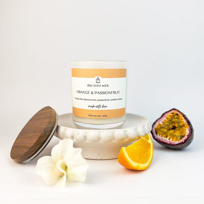 Orange & Passionfruit scented soy candle from The Violet Wick in glass jar with timber lid, orange slice and half a passionfruit., 250g.