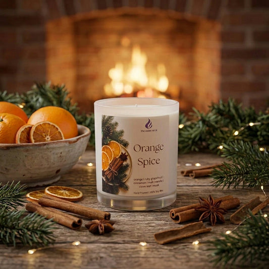 Orange Spice soy candle by The Violet Wick on coffee table with bowl of oranges and cinnamon sticks.