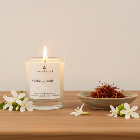 Candle labeled 'Cedar & Saffron' by 'the violet wick' on a wooden surface with a white background