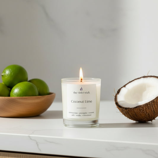 Coconut Lime candle with a white label on a white kitchen bench with limes and half a coconut