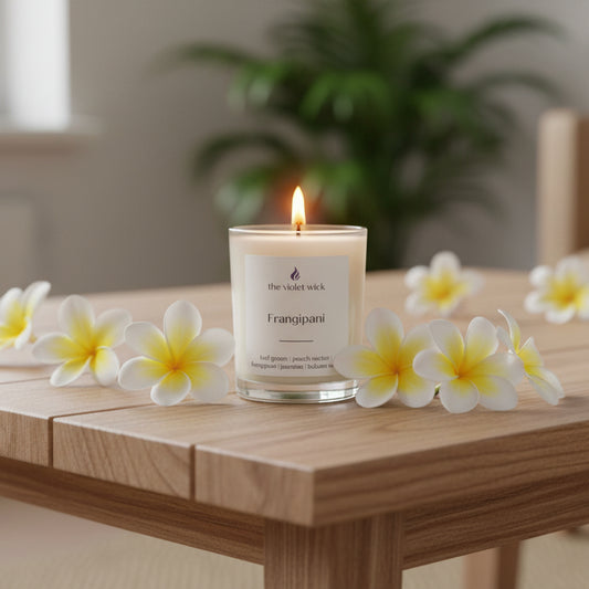 Candle with 'Frangipani' label on a coffee table with frangipani flowers.
