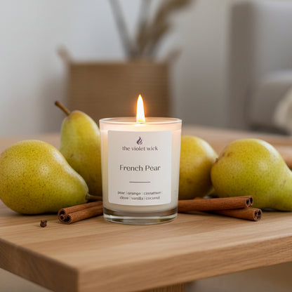 Candle labeled 'French Pear' by 'the violet wick' on a coffee table with pears and cinnamon sticks