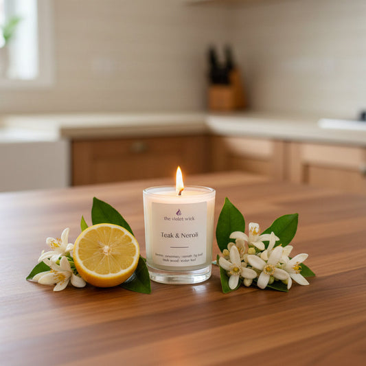 Candle labeled 'Teak & Neroli' on a wooden kitchen bench with lemon and neroli flowers