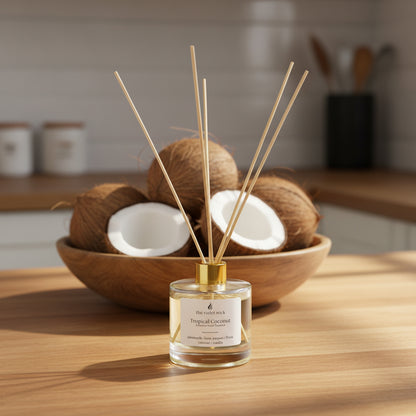 clear diffuser bottle with gold lid on a wooden kitchen bench with a bowl of coconuts in background