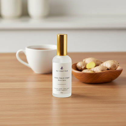 white room spray bottle labeled White Tea & Ginger on a timber table, cup of tea and bowl of ginger