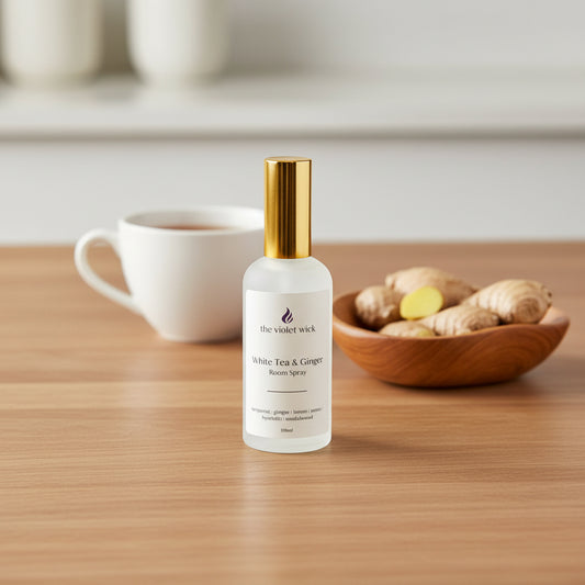 white room spray bottle labeled White Tea & Ginger on a timber table, cup of tea and bowl of ginger